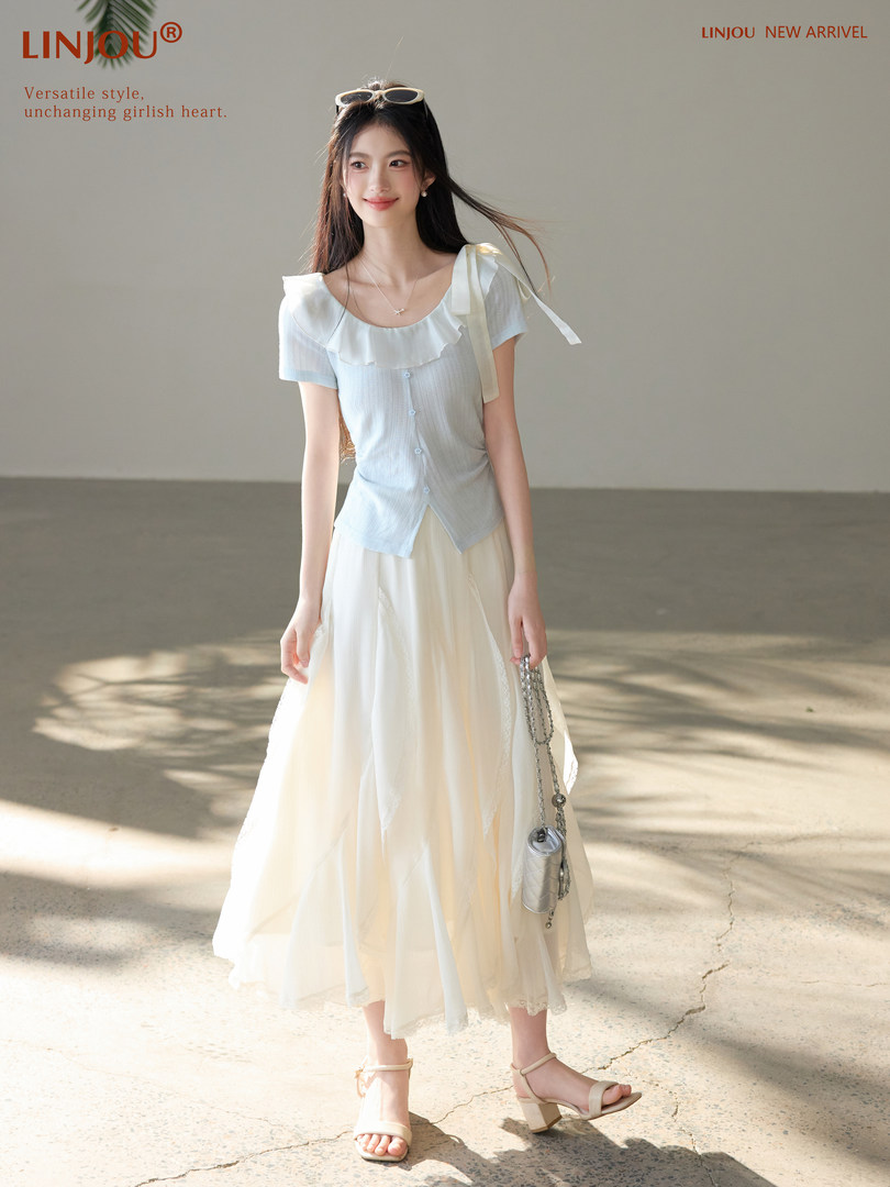Model wearing a light blue ruffled short-sleeve top with a flowing cream skirt