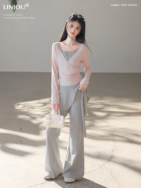 Model wearing a pink wrap top with gray wide-leg pants and a small handbag