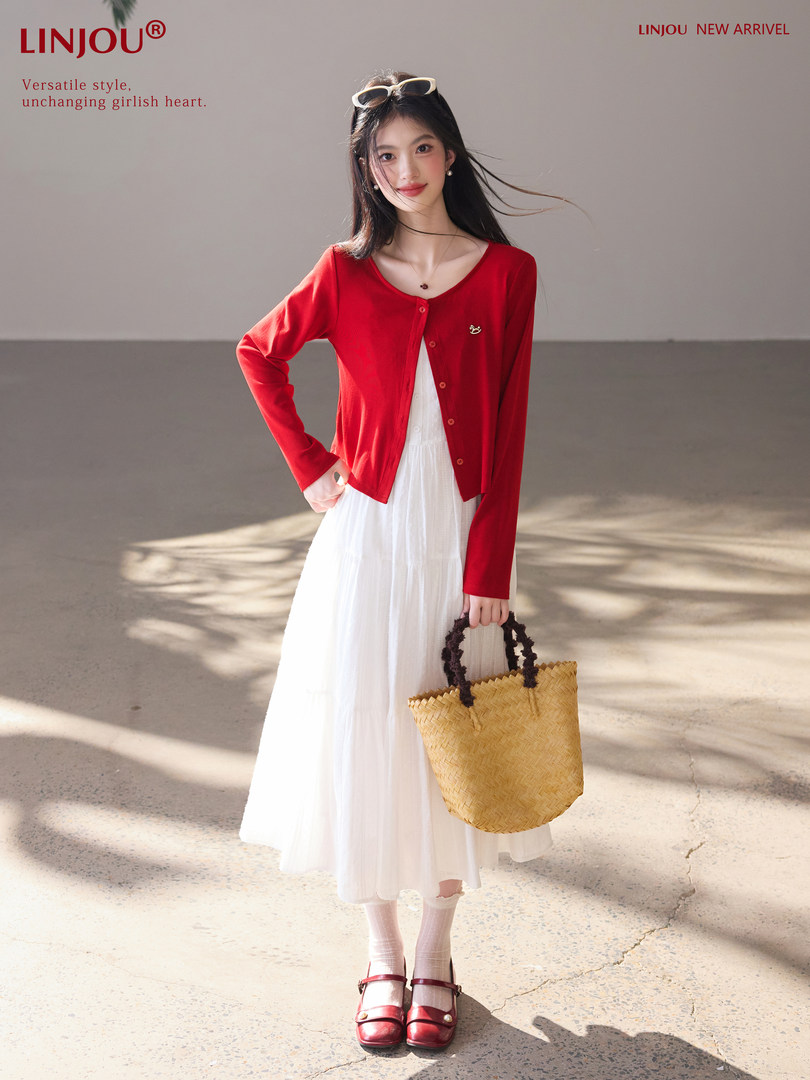 Model wearing a red cardigan over a white dress with a straw tote and red Mary Jane shoes
