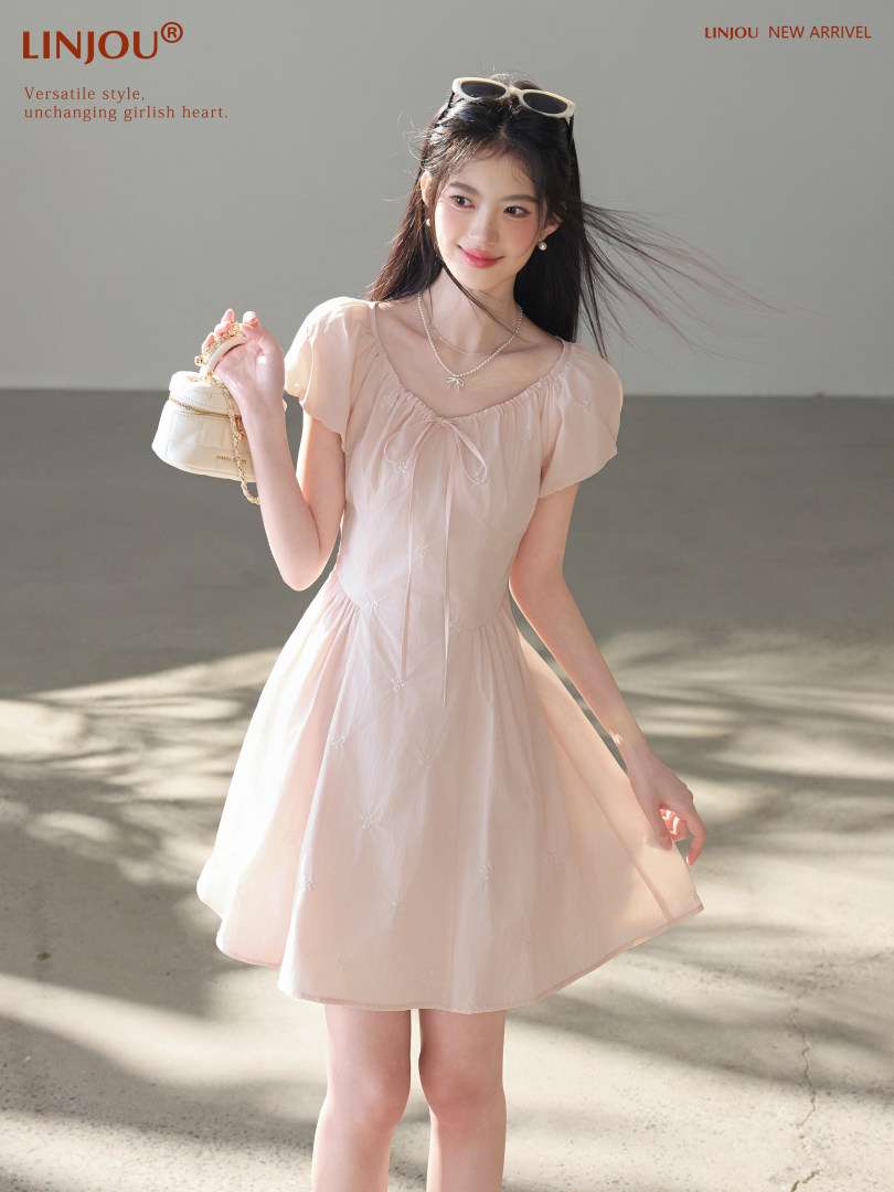 Model wearing a light pink short-sleeve dress with a small handbag