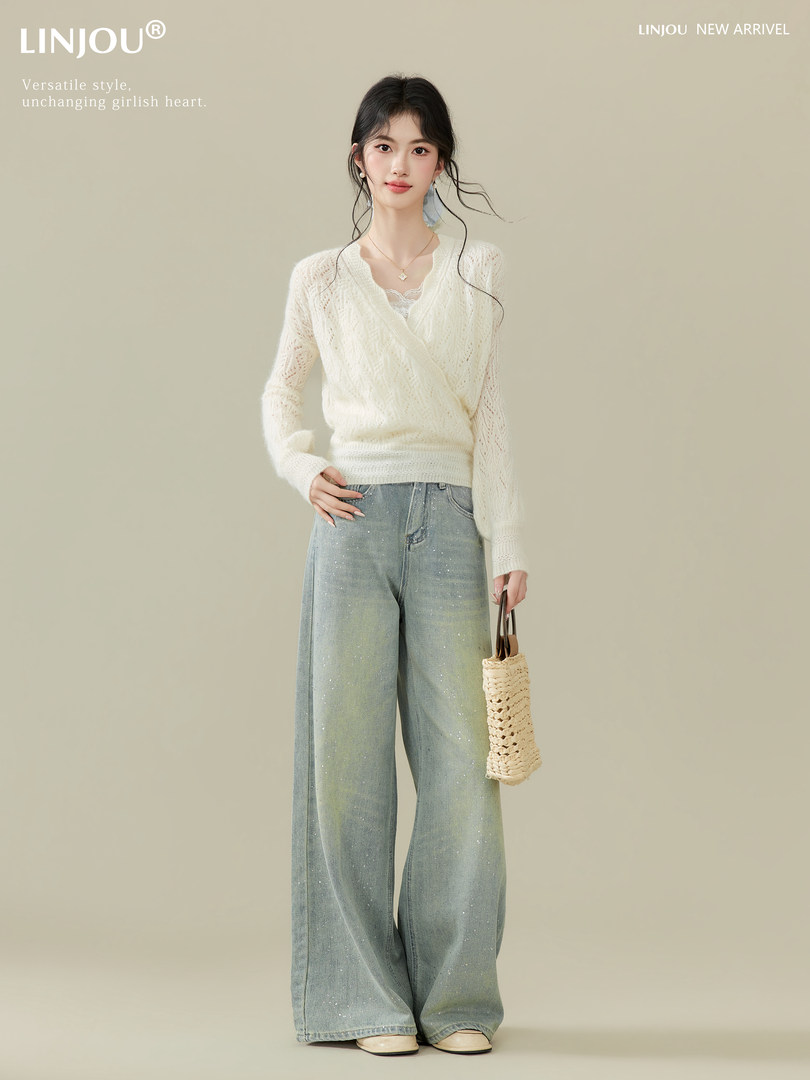Woman modeling a cream knit wrap sweater with wide-leg light blue jeans and a woven handbag.
