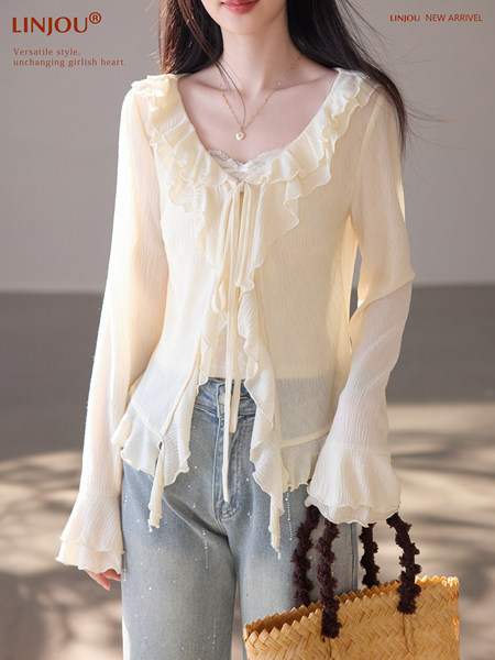 Model wearing a cream ruffled long-sleeve blouse with jeans and a woven bag