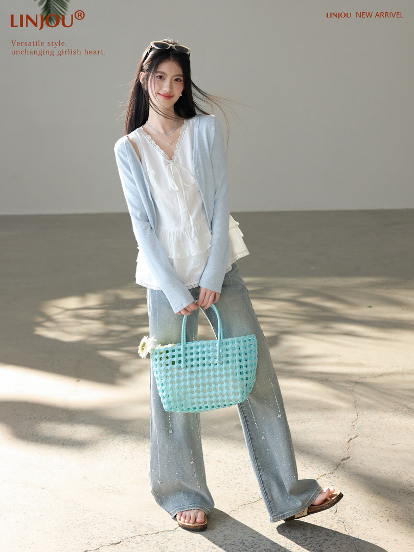 Fashion model wearing a white top, light blue cardigan, wide-leg jeans, and carrying a woven tote bag