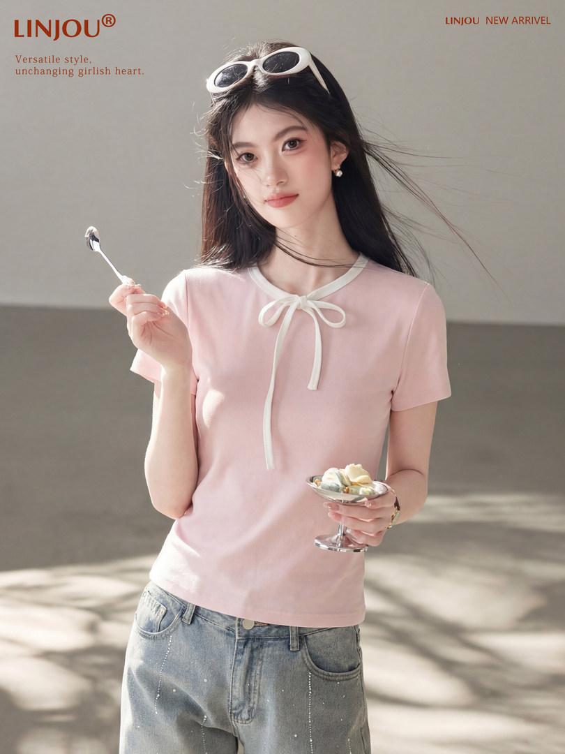 Model wearing a light pink short-sleeve top with white bow detail and jeans