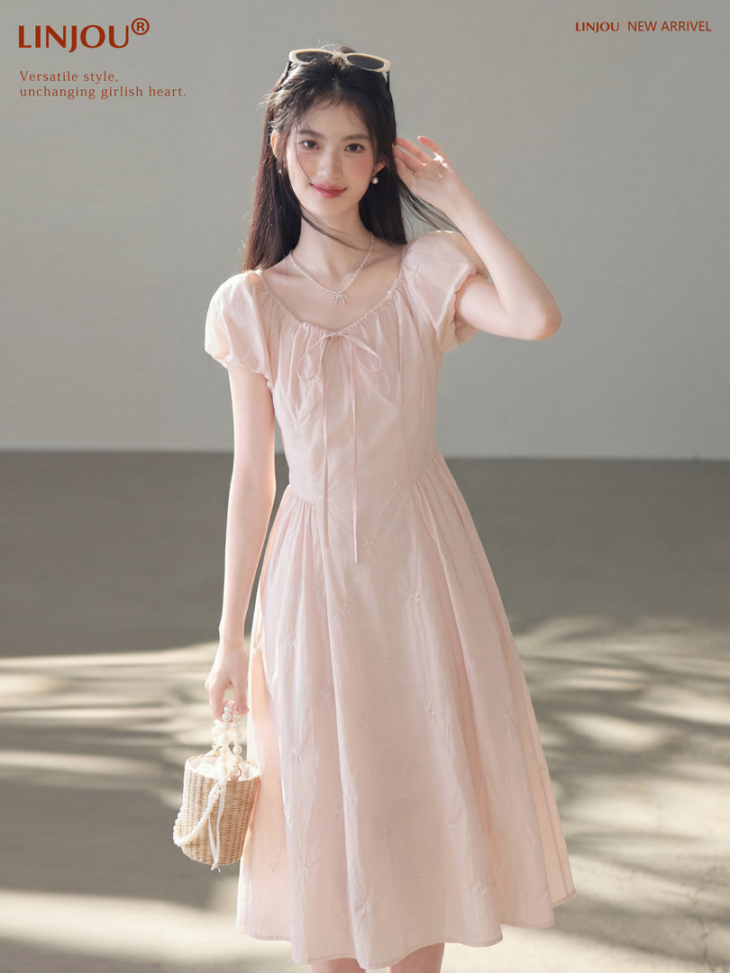Model wearing a light pink puff-sleeve midi dress and holding a small woven handbag