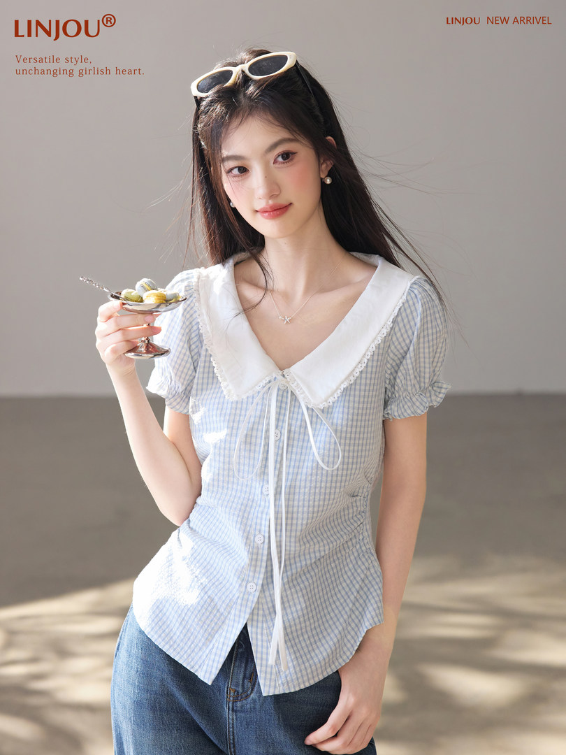 Model wearing a light blue gingham short-sleeve blouse with a large white collar