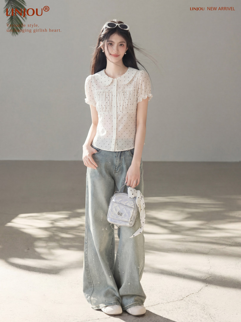 Female model wearing a white polka dot blouse with wide-leg jeans and a small silver handbag