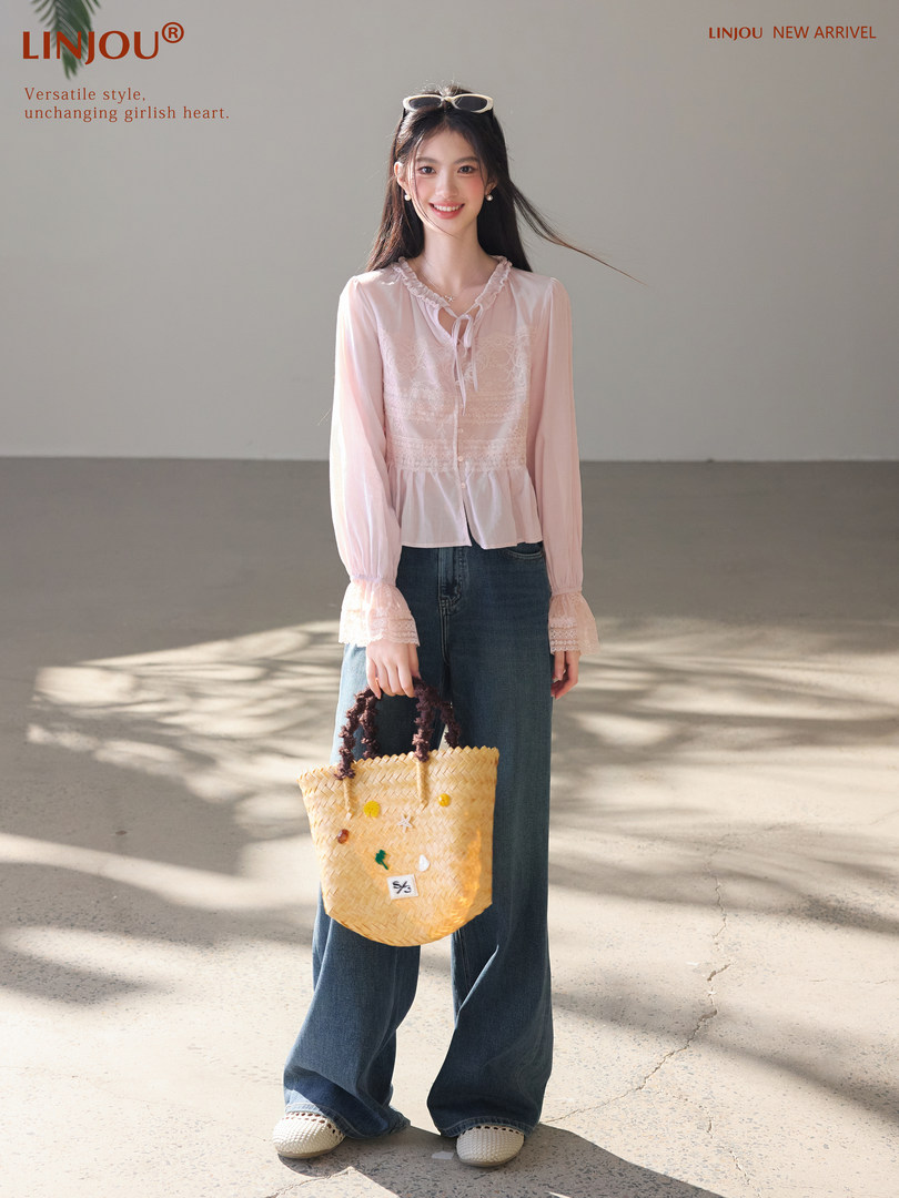 Model wearing a light pink sheer lace blouse with wide-leg jeans and a woven tote bag