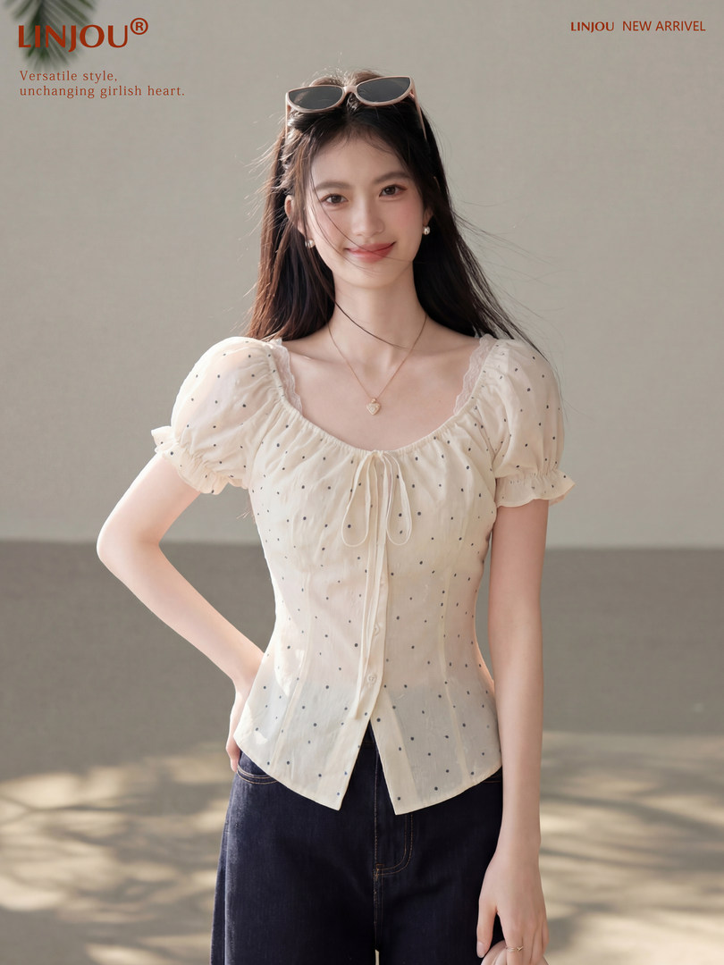 Model wearing a white short-sleeve polka dot blouse with a front tie detail