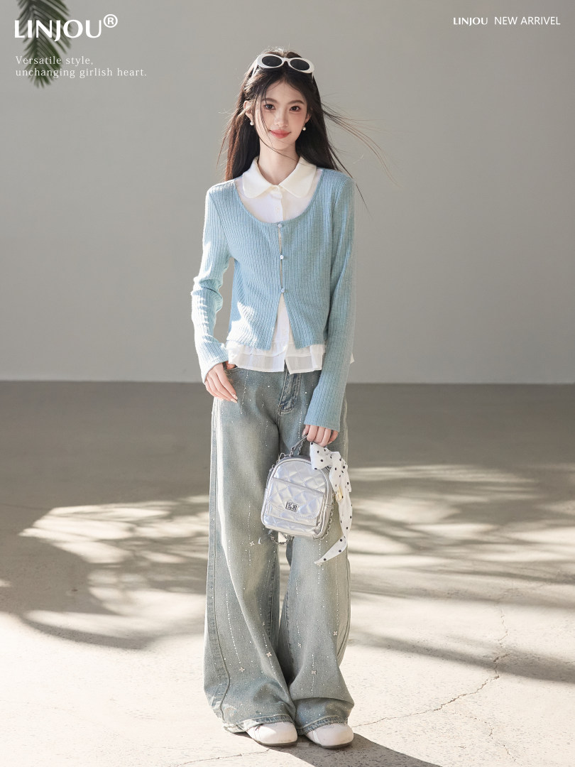 Model wearing a light blue cardigan layered over a white blouse with wide-leg jeans, holding a small silver bag.