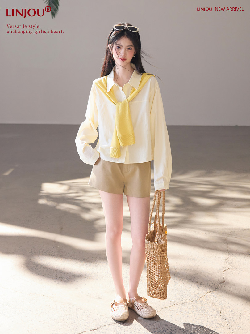 Model wearing a light summer outfit with white shirt, yellow sweater, beige shorts, woven bag and sandals
