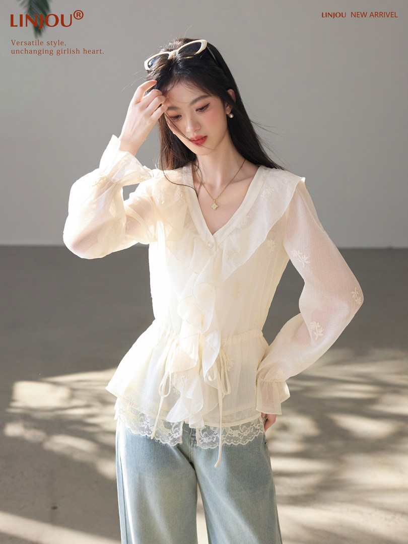 Model wearing a sheer cream long-sleeve blouse with ruffle details and jeans