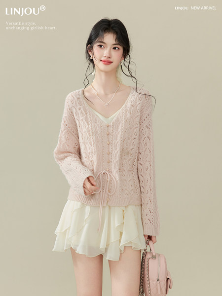 Model wearing a light pink lace knit cardigan over a cream ruffled skirt with a matching handbag