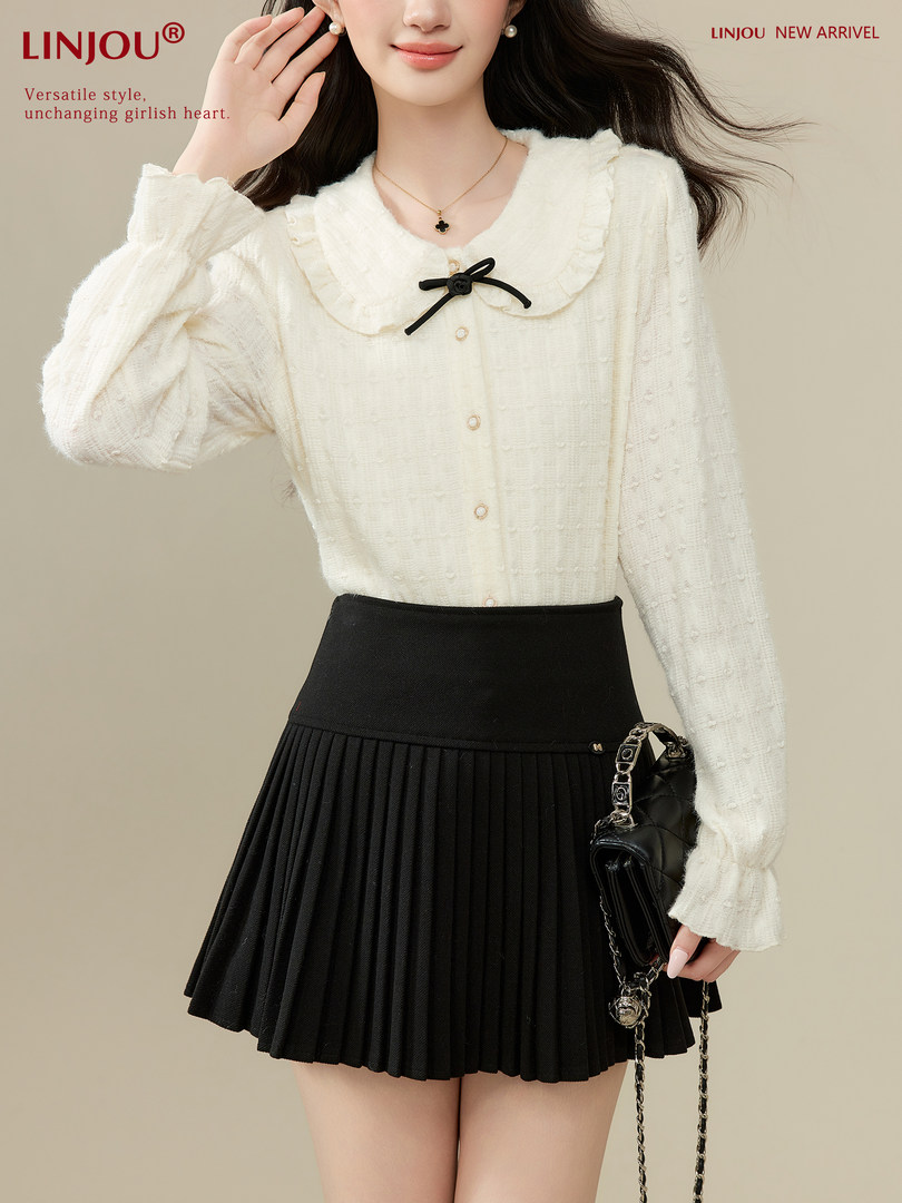 Model wearing a cream ruffled blouse with a black pleated skirt and handbag