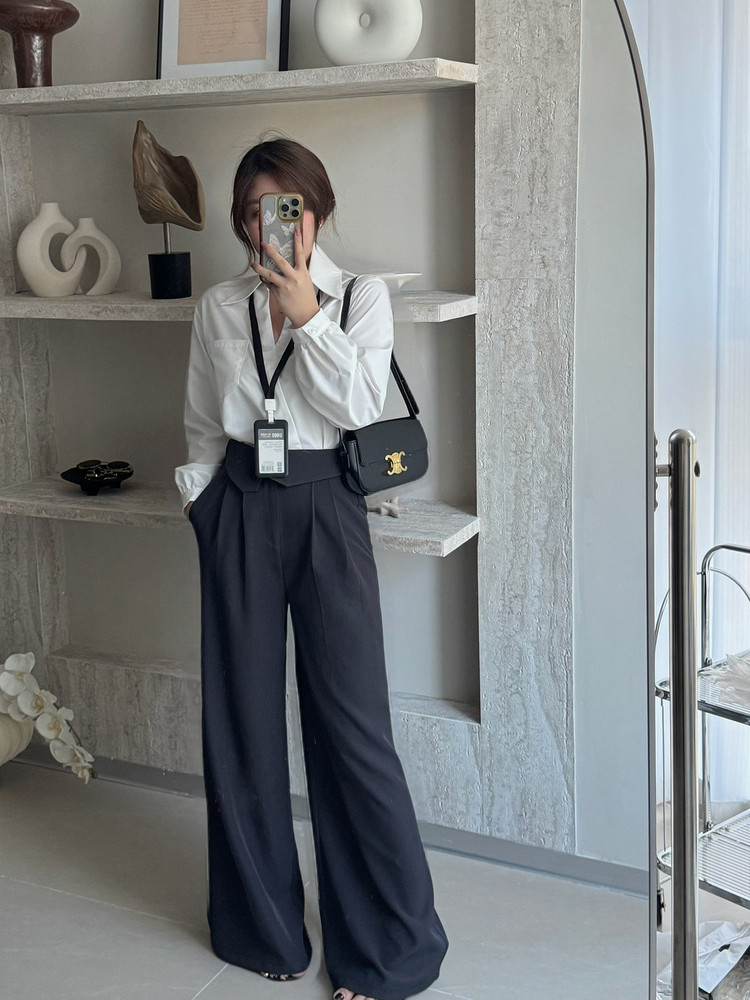 Model wearing a white button-up shirt, dark wide-leg trousers, and a black shoulder bag