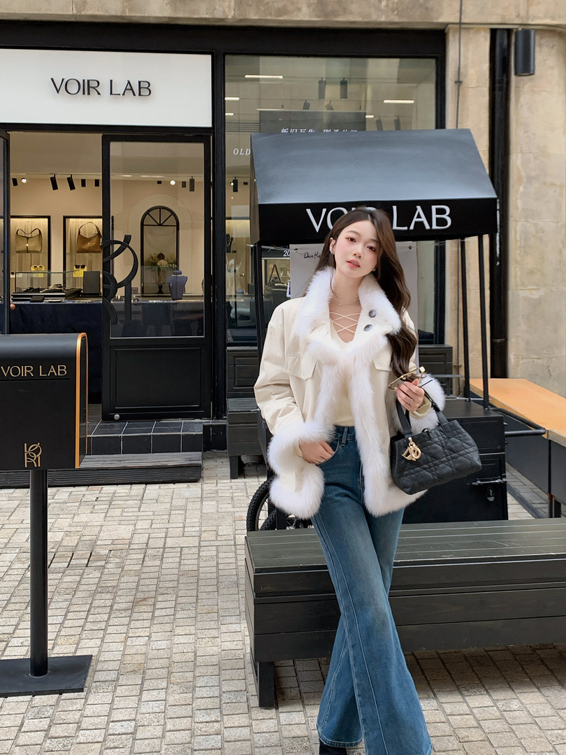 Woman wearing a white fur-trimmed jacket with blue jeans and a black quilted handbag