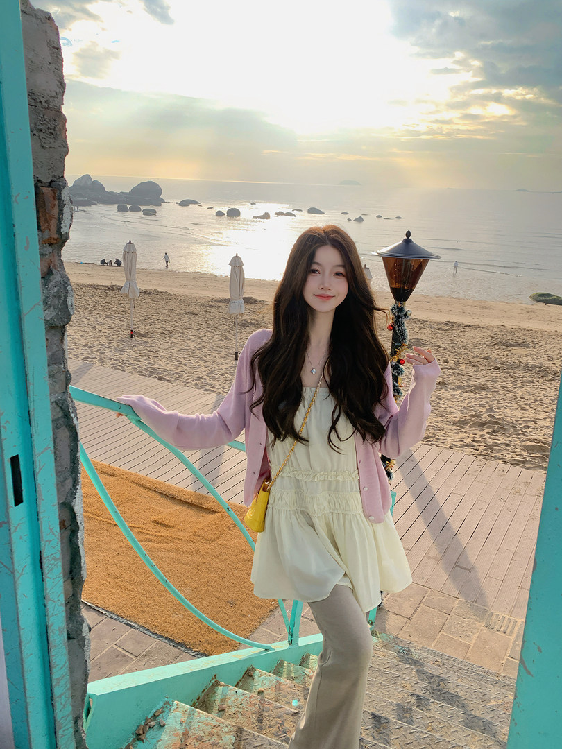 Woman wearing a pastel cardigan and cream dress on a beach