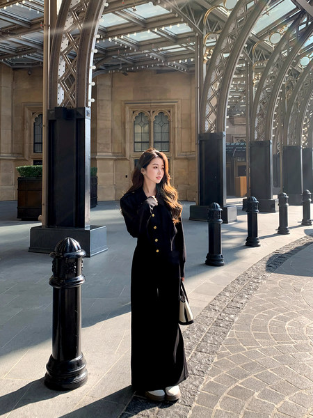 Woman wearing a long black buttoned outfit with gold buttons and a handbag