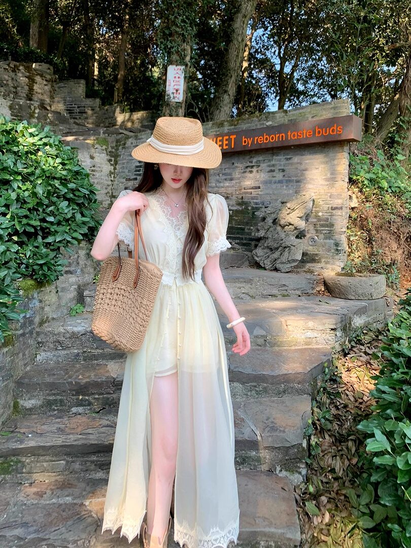 Woman wearing a light cream lace maxi dress with straw hat and woven tote bag outdoors