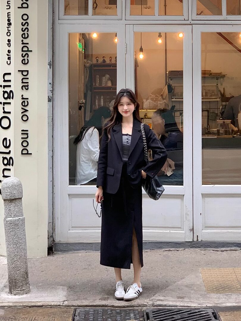 Woman wearing a black blazer and skirt outfit with white sneakers outside a cafe