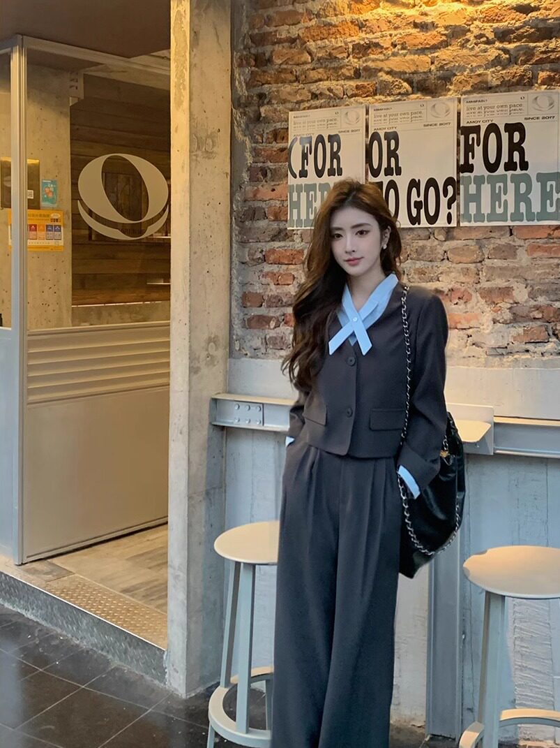 Woman wearing a dark gray suit set with a light blue bow detail and black shoulder bag