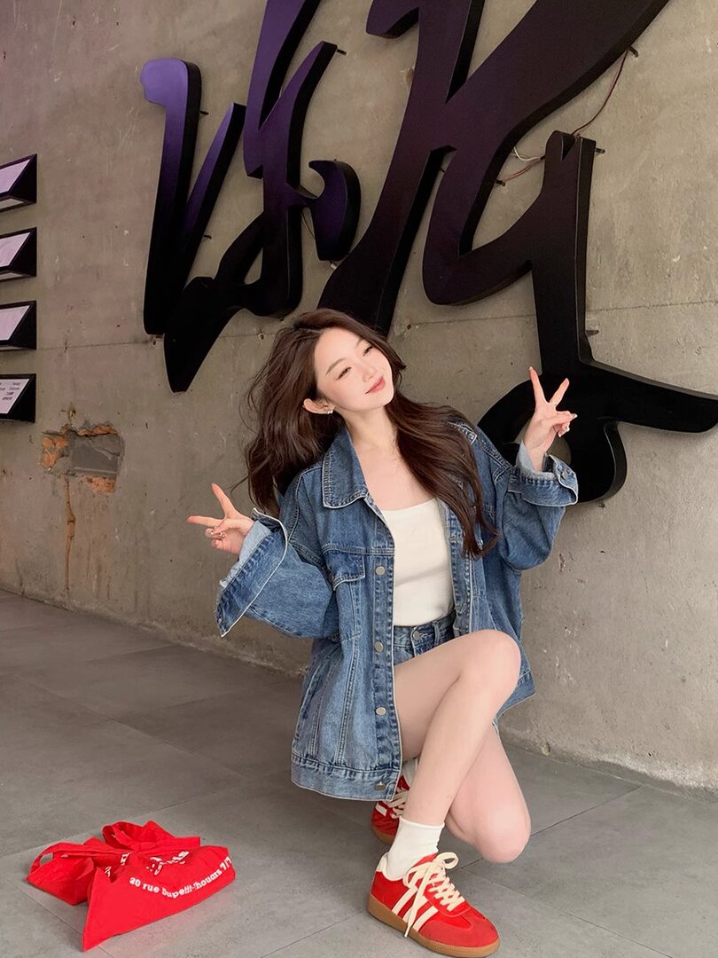 Woman wearing an oversized denim jacket with white top and red sneakers