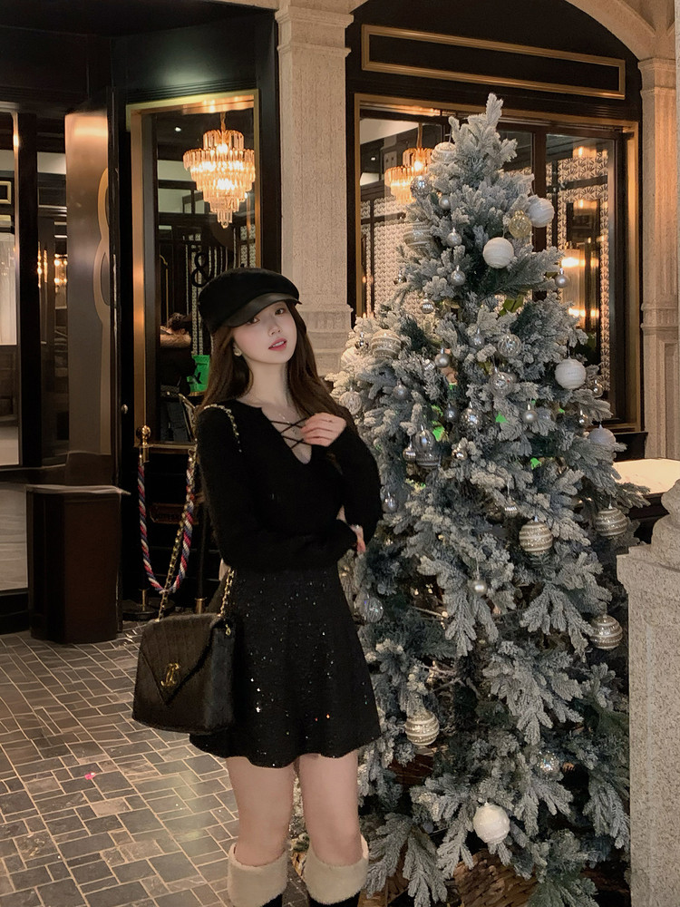 Woman wearing a black long-sleeve top and sparkly black skirt with a black hat and handbag