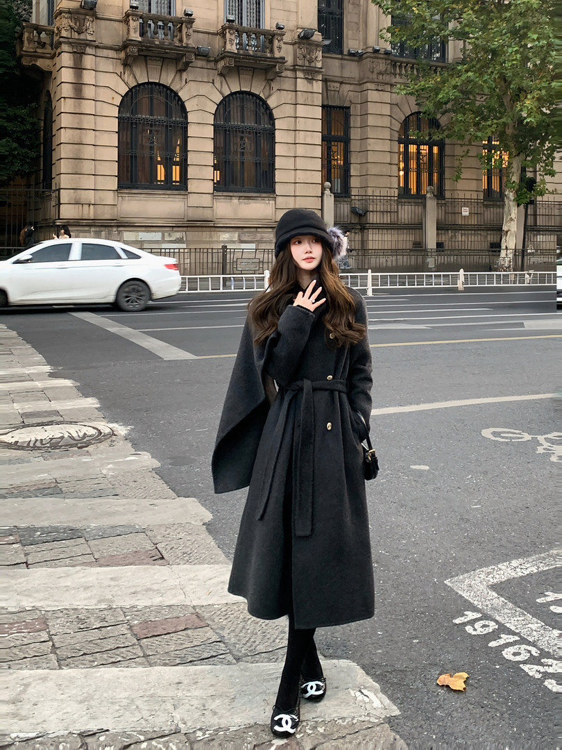 Woman wearing a long black belted coat and black hat on a city street