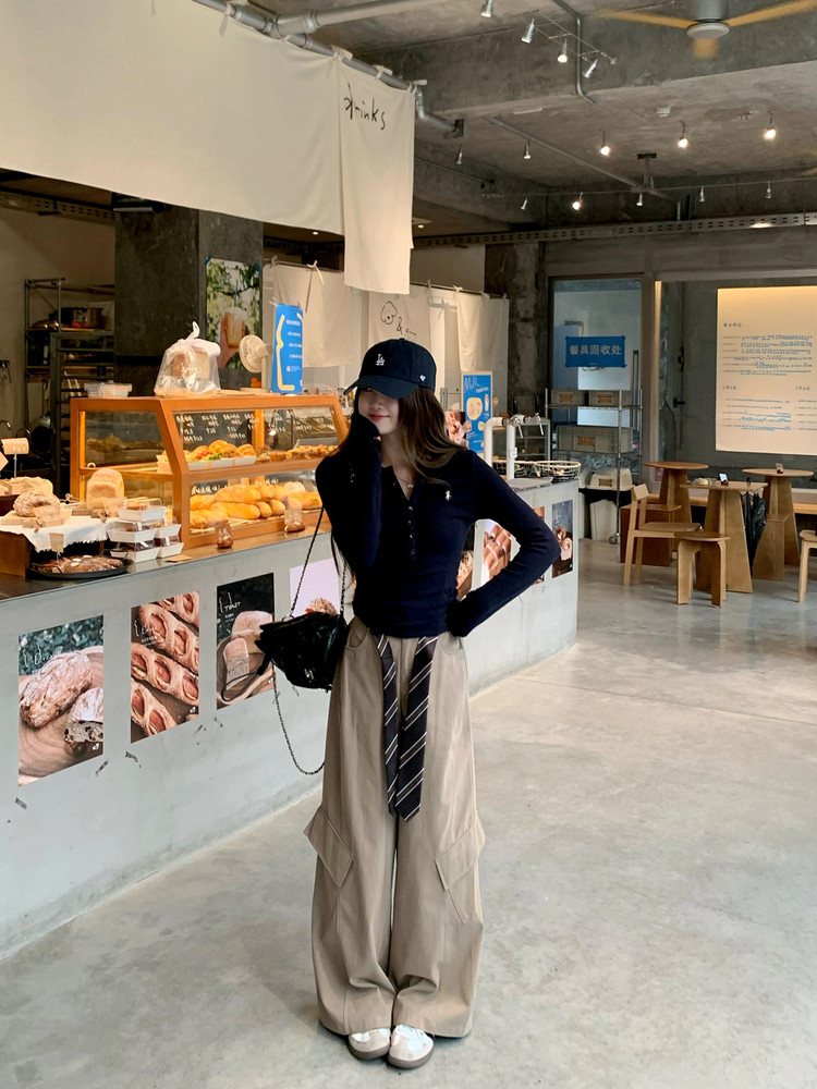 Model wearing a navy top with beige wide-leg cargo pants and a tie in a cafe