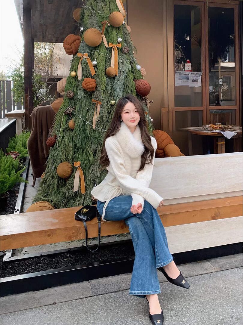 Woman wearing a white knit sweater and flared blue jeans seated outdoors