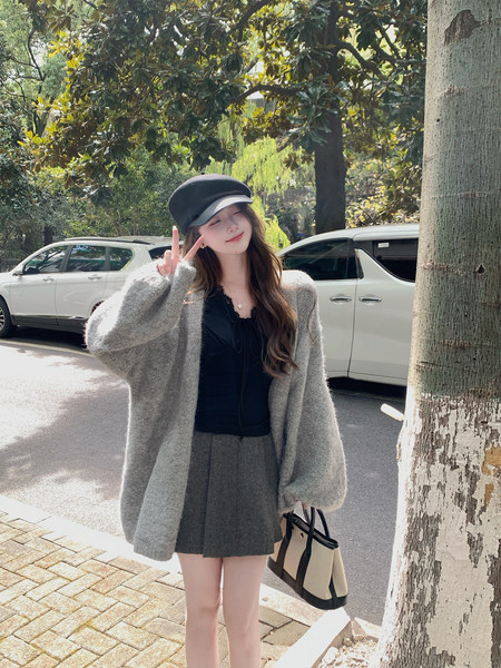Woman wearing a gray oversized cardigan and pleated skirt with a black cap and tote bag outdoors
