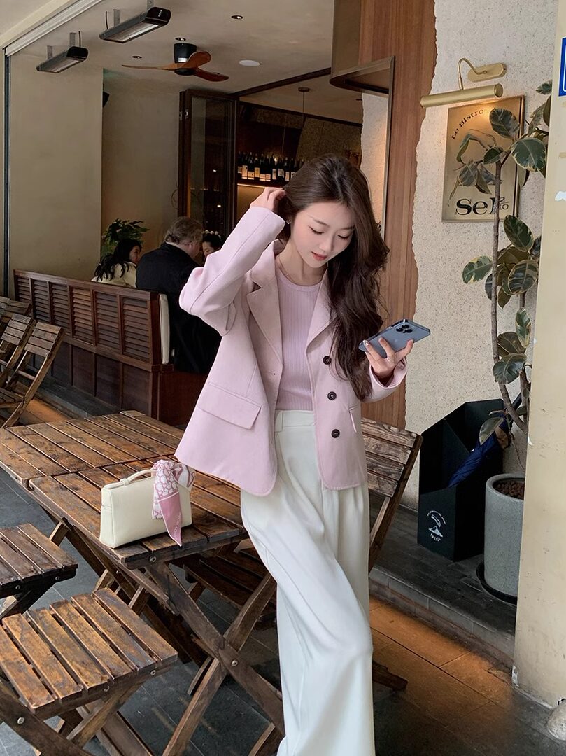 Woman wearing a light pink blazer and white wide-leg pants in a cafe
