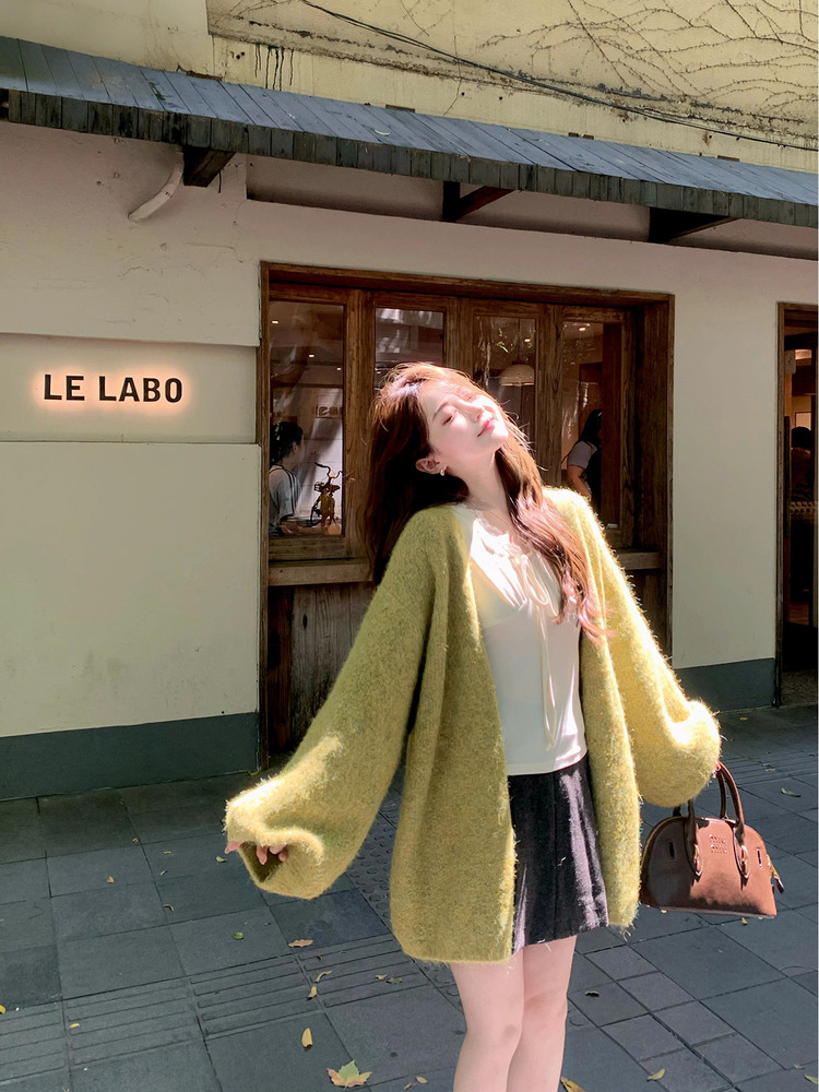 Woman wearing a fuzzy oversized green cardigan with a white top and dark skirt outdoors