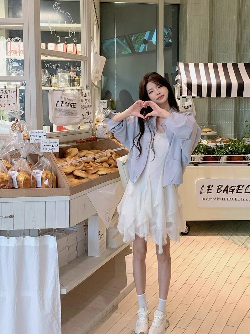 Woman wearing a white dress with a light lavender shirt in a bakery setting