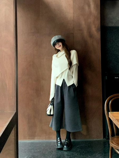 Woman modeling a chic layered winter outfit with hat, wide-leg bottoms, and loafers