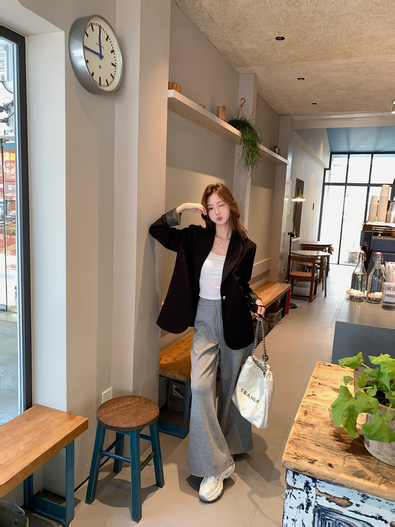 Woman wearing a black blazer, white top, gray wide-leg pants, and sneakers in a cafe