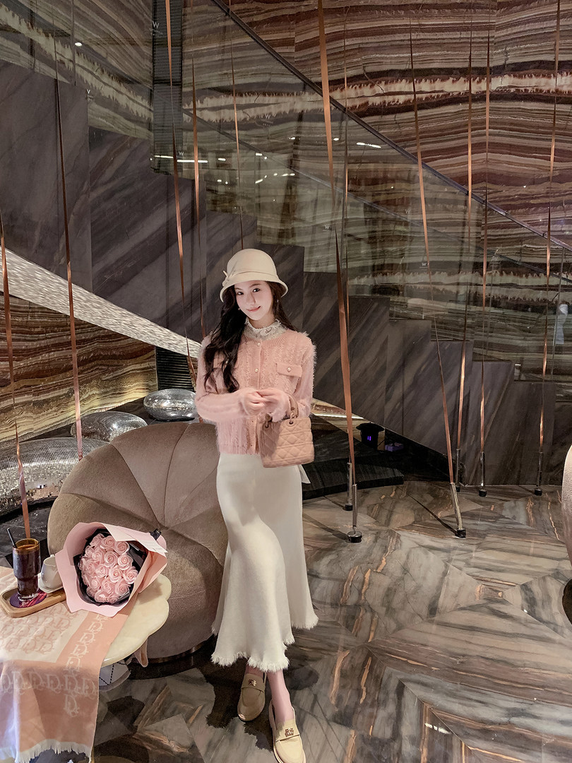 Woman wearing a pink textured cardigan, cream long skirt, hat, and quilted handbag