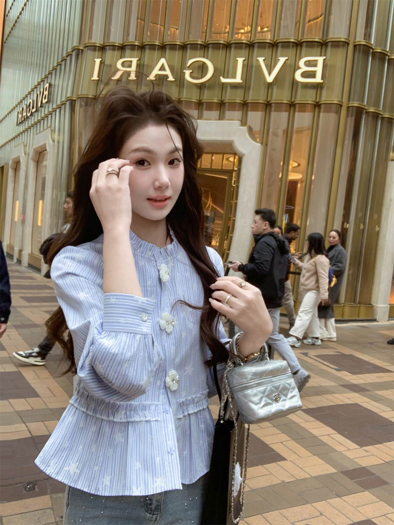 Woman wearing a light blue striped blouse and holding a silver quilted mini bag outside a BVLGARI store