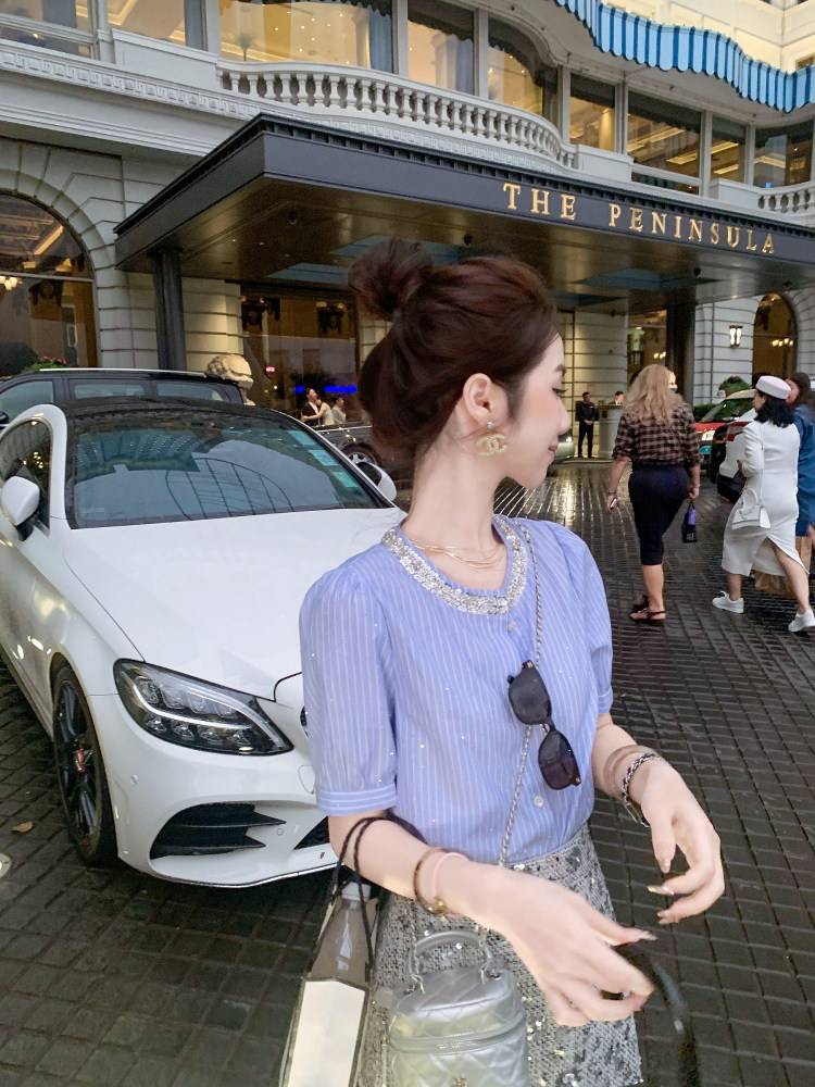 Woman wearing a light blue striped blouse and patterned skirt with a small handbag