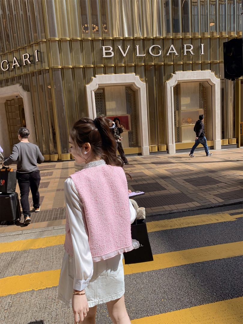 Woman wearing a pink textured vest over a white outfit on a city street