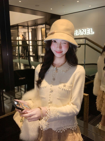 Woman wearing a cream knit cardigan and matching cloche hat in a luxury boutique.