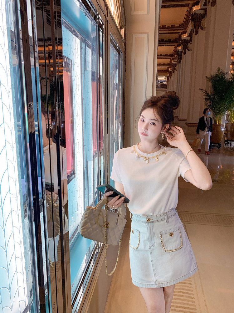 Woman wearing a white short-sleeve top, light denim skirt, and quilted handbag