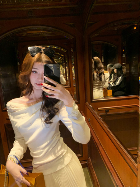 Woman wearing a white off-shoulder long-sleeve top with a pleated skirt in a mirror selfie