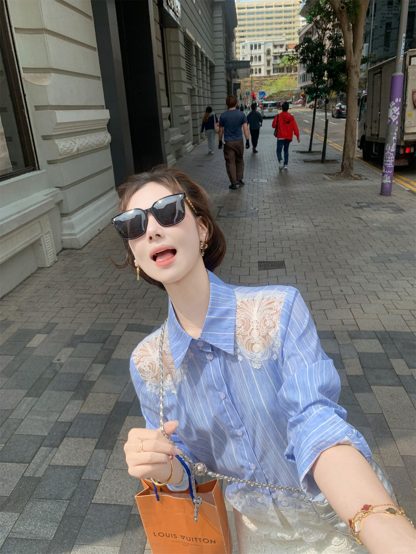 Woman wearing a light blue striped blouse with lace details, sunglasses, and a Louis Vuitton bag outdoors