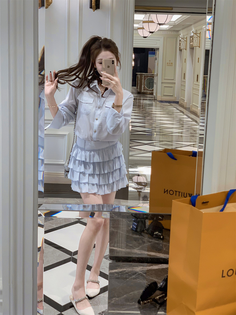 Woman wearing a light blue ruffled skirt and white blouse in a mirror selfie