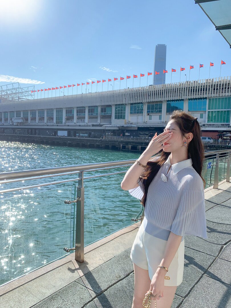 Woman wearing a white pleated blouse and shorts outdoors by the water