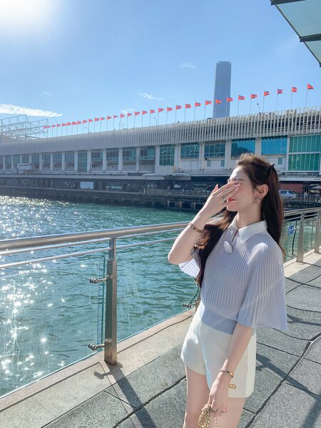 Woman wearing a white pleated blouse and shorts outdoors by the water
