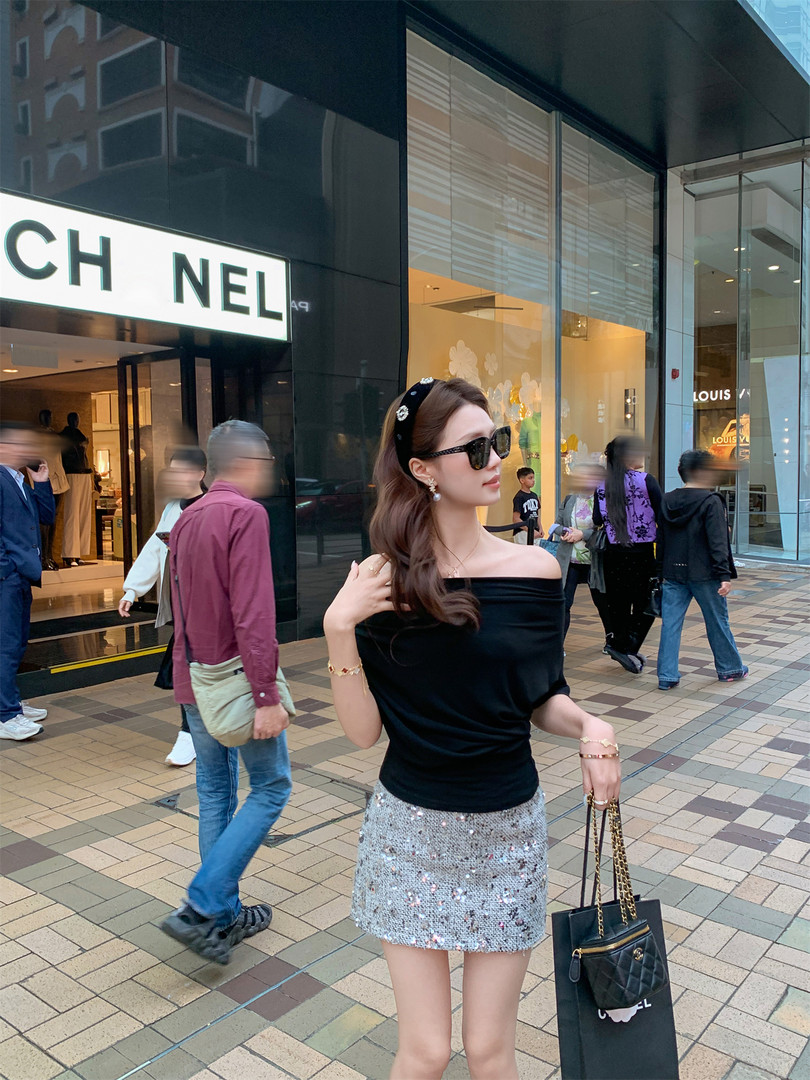 Woman wearing a black off-shoulder top with a silver sequin mini skirt and black handbag outside a Chanel store