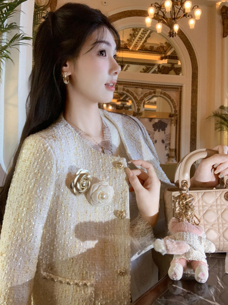 Model wearing a cream tweed jacket and holding a quilted handbag