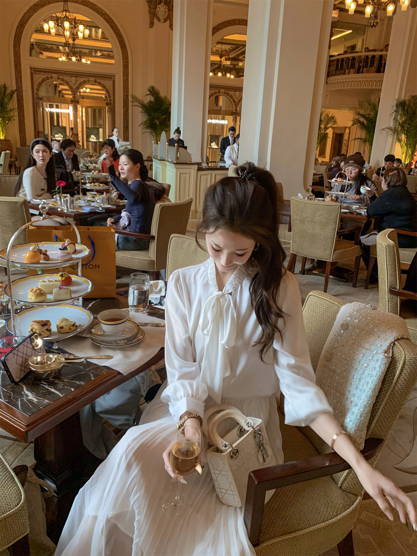 Woman wearing a white elegant dress with a cream handbag at a luxury restaurant